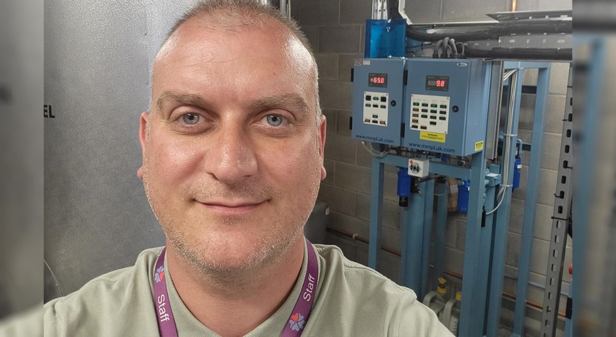 Andy Dealy, male with blue eyes and khaki t shirt pictured in front of a machine control panel.